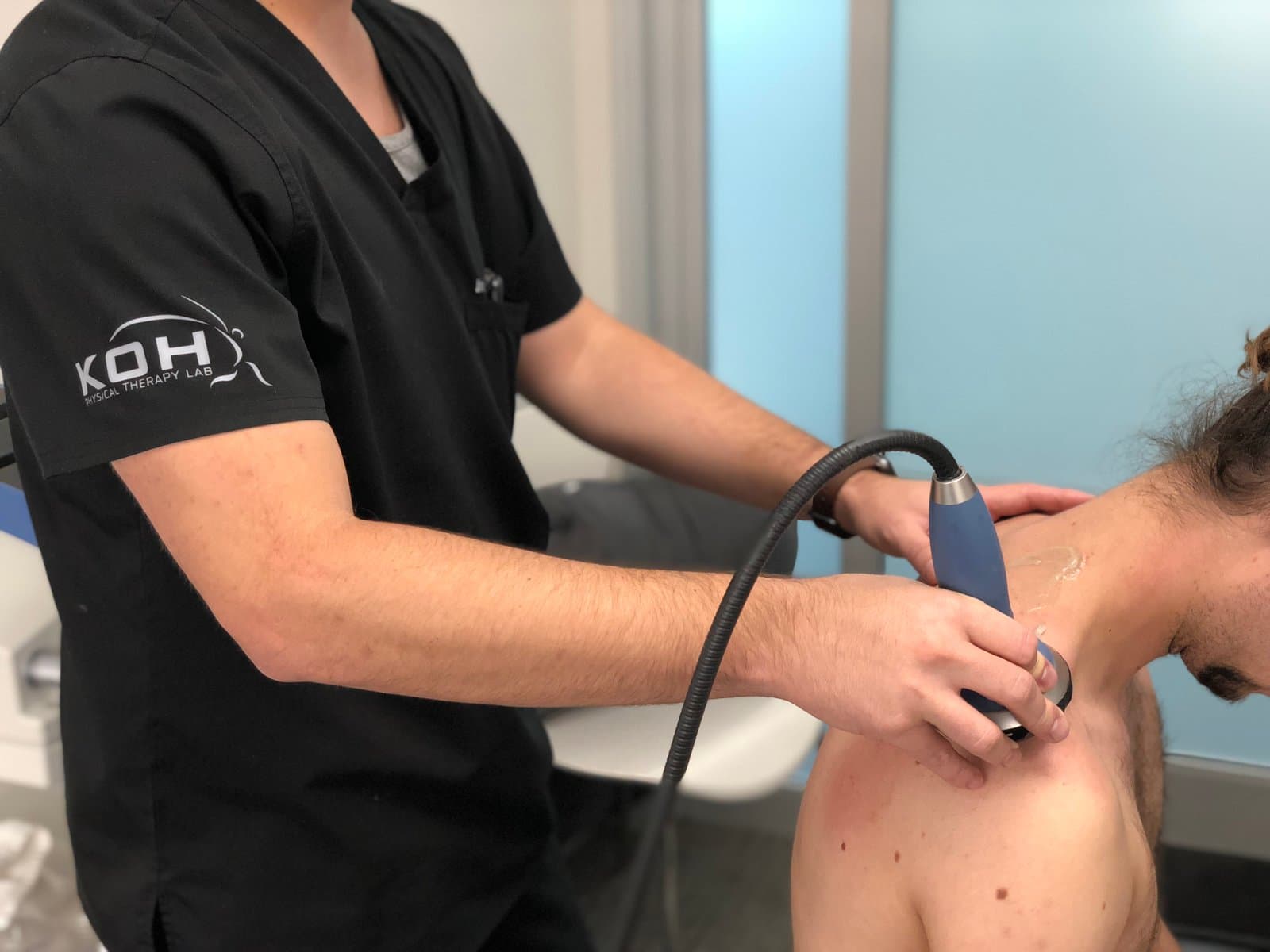 A KOH Physical Therapy Lab therapist applying focused shockwave therapy to a patient's upper shoulder with a handheld applicator